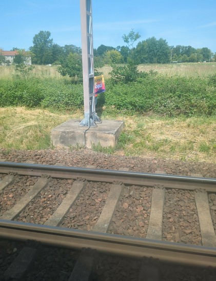 An einer Bahnstrecke wird hinter einem Mast eine Paulaner-Flagge hochgehalten.